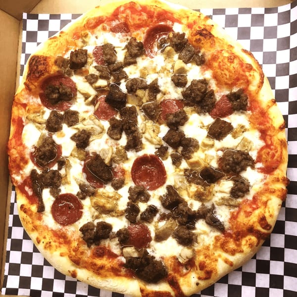 A BWP - Pizza Island pizza with pepperoni, sausage, and mushrooms on a checkered paper liner.